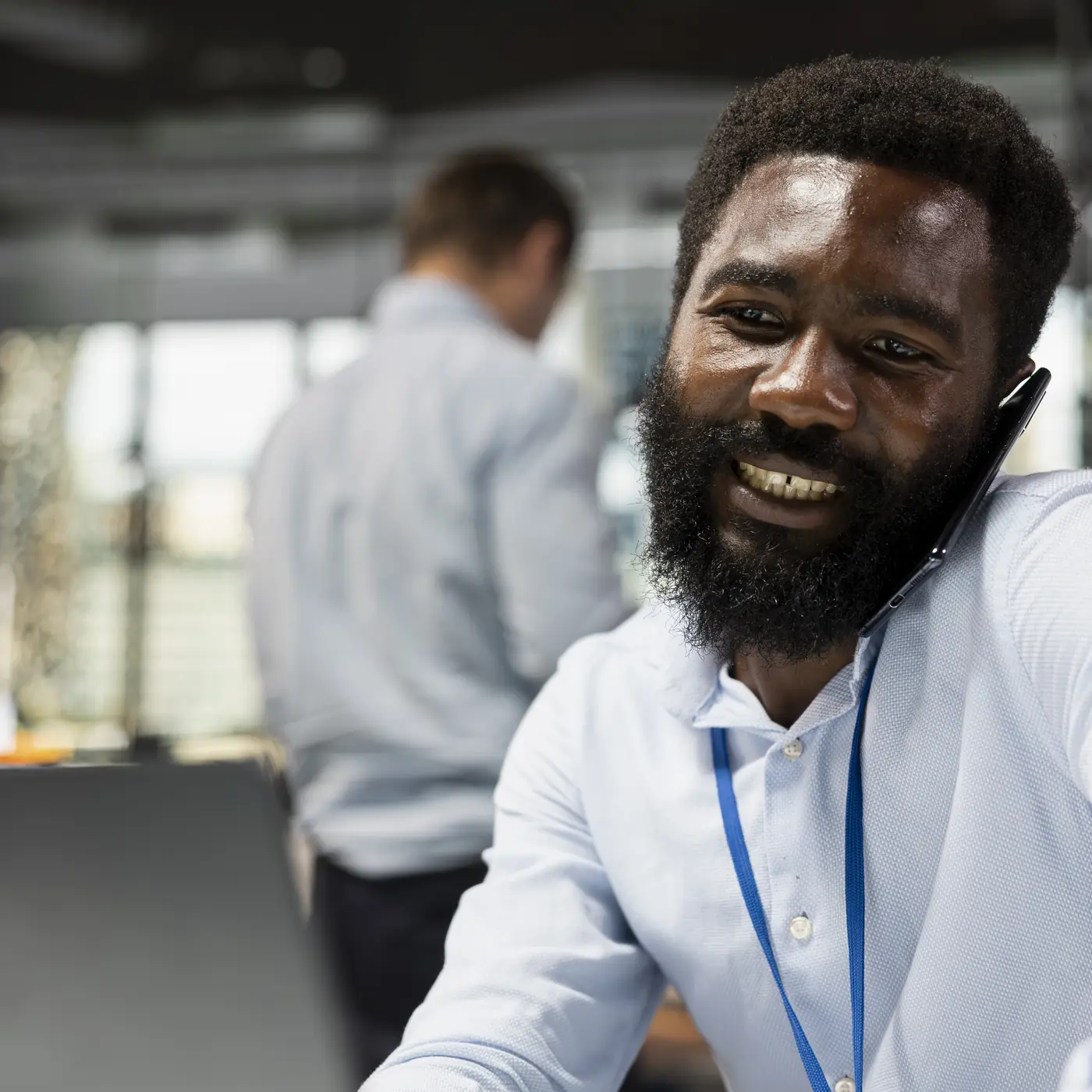 A smiling man on a phone call at his desk, with a laptop open in front of him